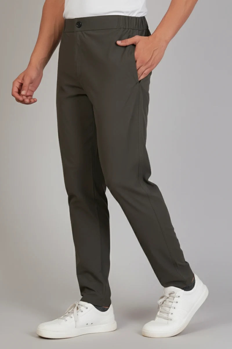 Person wearing dark gray pants and white sneakers on a plain background
